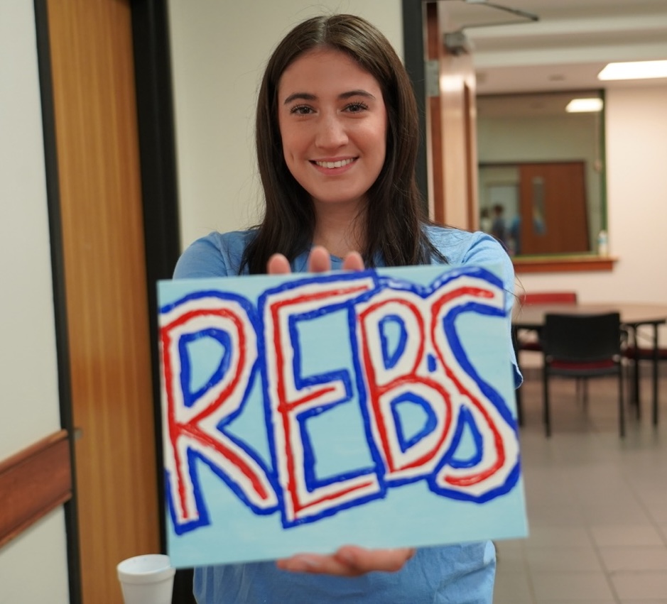Student holding their painting that says rebs.