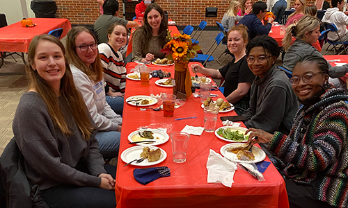 Seven students sit together at a table enjoying a dinner