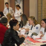 Pharmacy students sit at a table and talk with patients at a health fair.