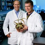 David Pasco and Nirmal Pugh holding an aloe plant while wearing lab white coats.