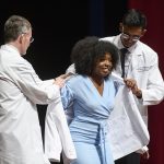 A female student is assisted with her white coat from school's dean and student body representative