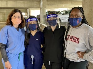 Three female students and an administrator stand together wearing face masks.