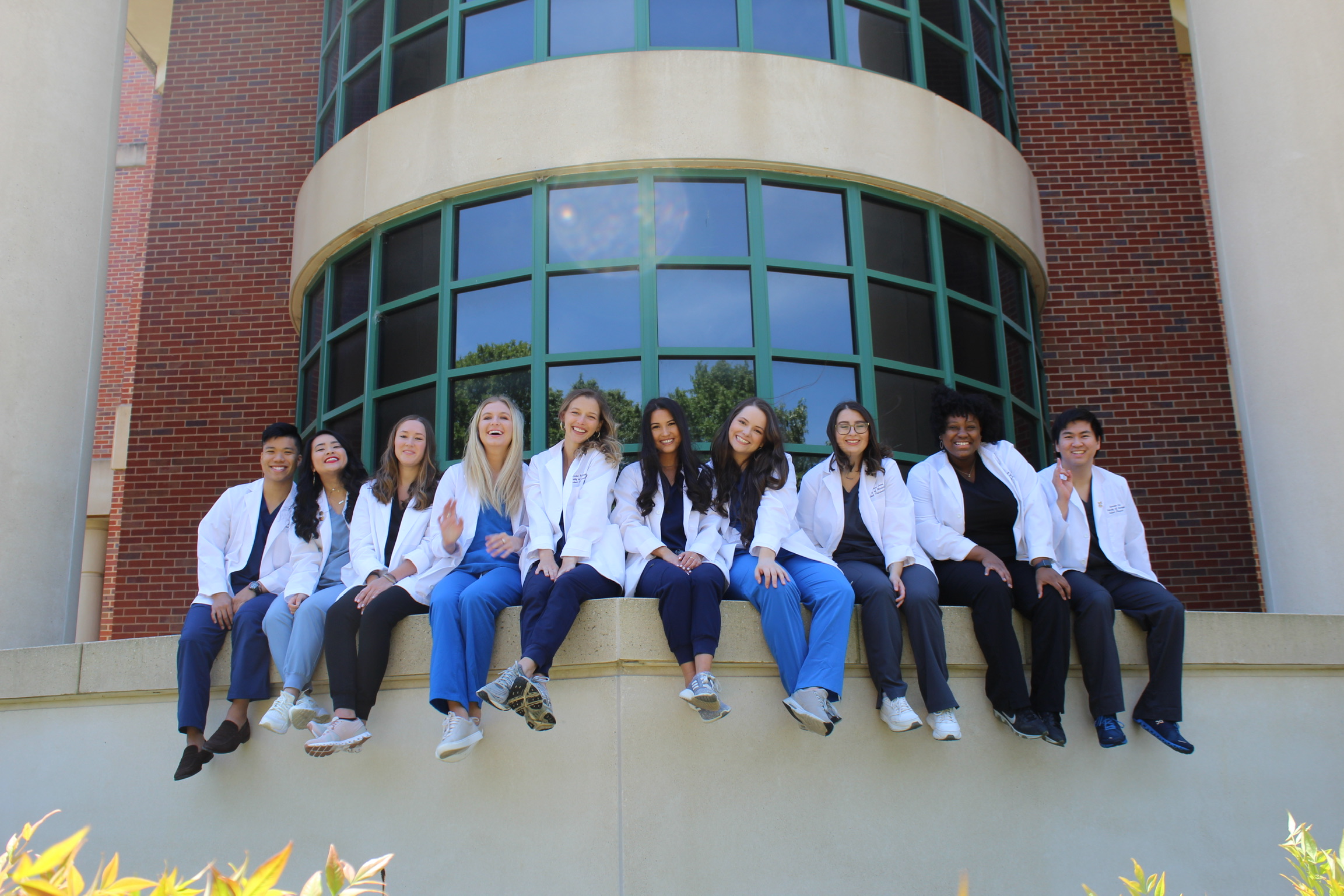 10 pharmacy students sit on ledge in front of school building