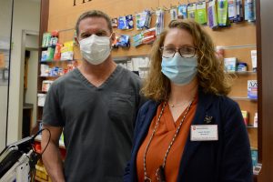 Pharmacists Sandy and Chad stand behind the pharmacy counter wearing masks.
