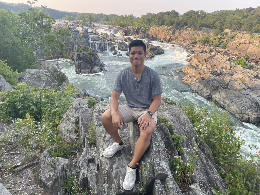 Eric Pham sits on a rock with river flowing behind him.