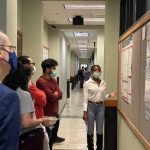 Graduate student showing poster to fellow students and faculty members
