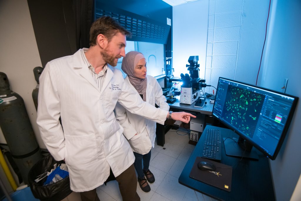 Jason Paris and a graduate student look at scientific results on a computer screen.