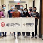 Group of graduate students in masks holding a sign